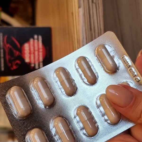 Strieborný blister Alpha Beast s béžovými kapsulami zblízka v ruke, čierno-červená krabička rozostrená v pozadí