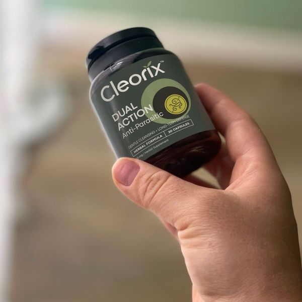 Jedna dóza Cleorix s čiernym uzáverom držaná šikmo v ruke, pozadie miestnosti je rozmazané