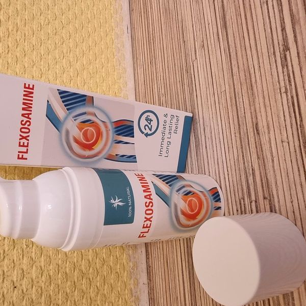 Biela fľaštička Flexosamine Gel s pumpičkou, vedľa nej odložený biely uzáver a bielo-tyrkysová krabička na drevenom podklade