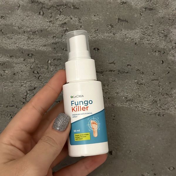 Biela fľaštička Fungokiller 50 ml s rozprašovačom pod priehľadným vrchnákom v ženskej ruke pred sivou stenou