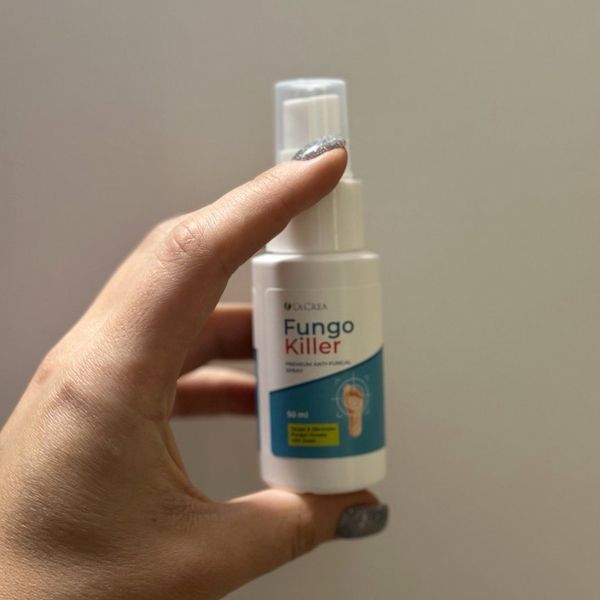 Fľaštička Fungokiller zovretá zvislo medzi palcom a ukazovákom ruky so striebristým trblietavým lakom na nechtoch