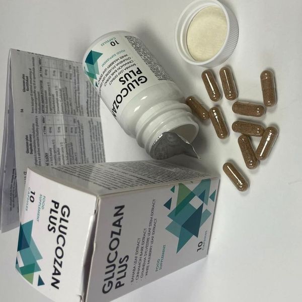 Prevrátená otvorená fľaštička Glucozan Plus, vysypané hnedé kapsuly, uzáver, krabička a rozložený príbalový leták