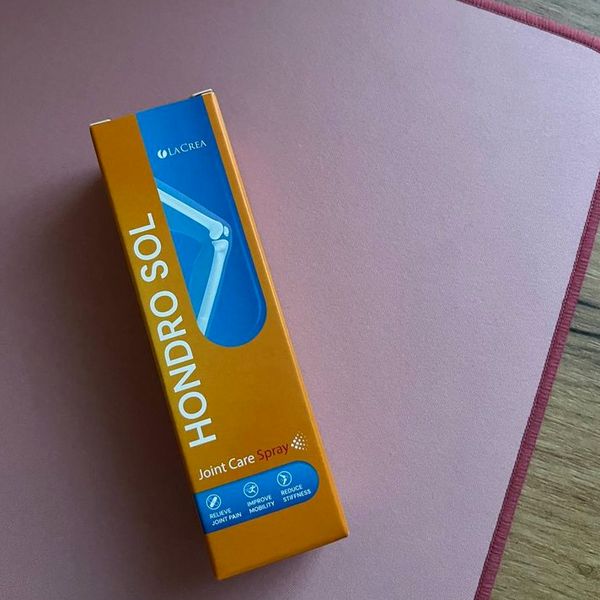Oranžová krabička Hondro Sol leží šikmo na ružovej podložke, vpravo dole vidno okraj dreveného stola