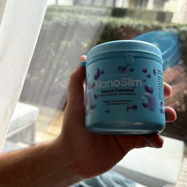 Svetlomodrá dóza Nano Slim s nápisom Zero Sugar a fialovými kvapkami na etikete, držaná v ruke pri okne s bielou záclonou