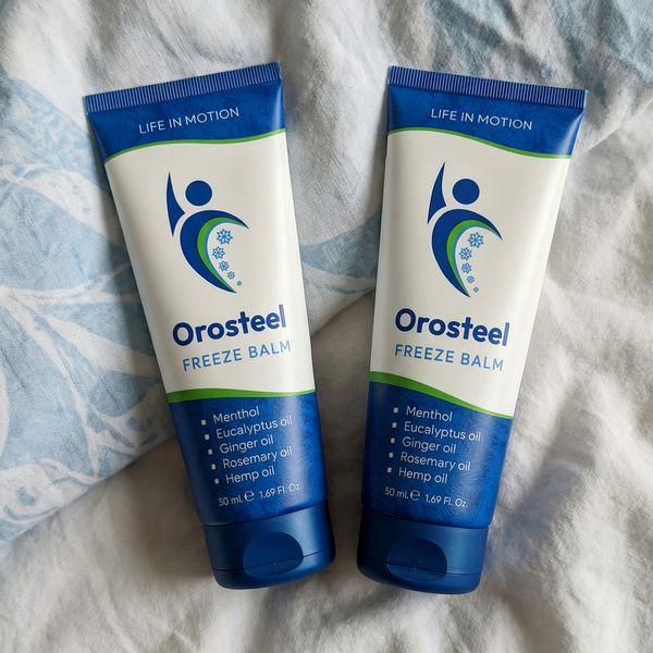Dve tuby Orosteel Freeze Balm s modrým uzáverom ležia vedľa seba na bielo-modrej posteľnej bielizni