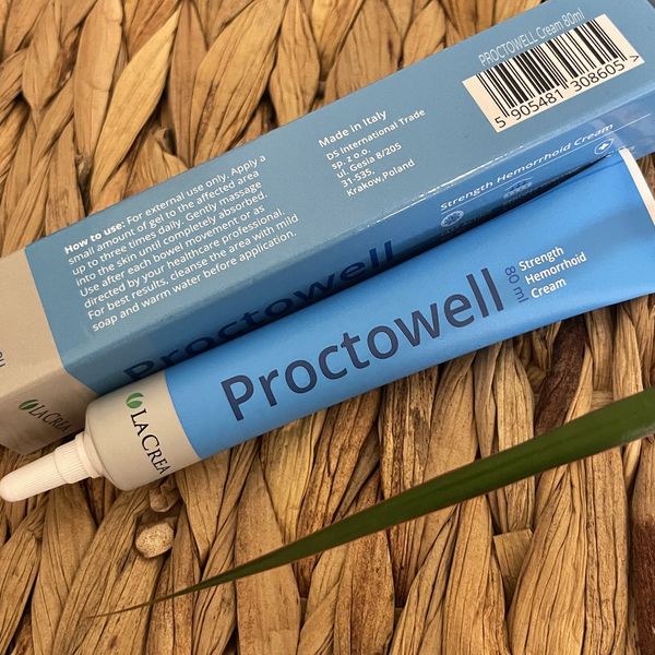 Modrá tuba Proctowell 80 ml s bielym aplikátorom a modrá krabička s návodom položené na pletenej slamenej podložke