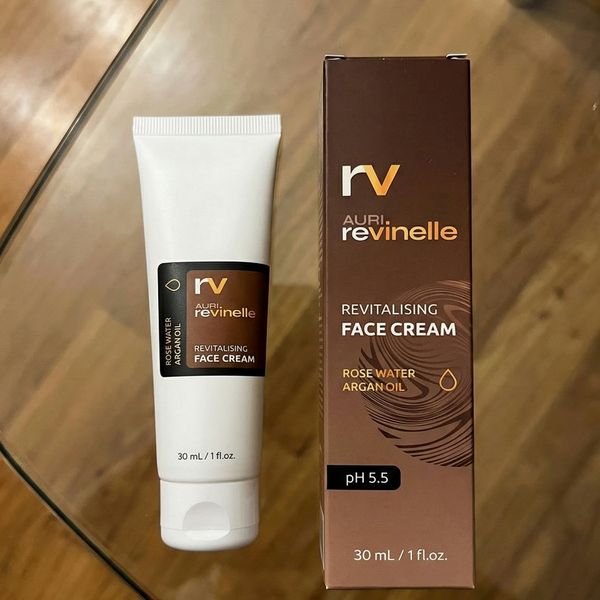 Biela tuba Revinelle s hnedou etiketou leží vedľa hnedej krabičky s nápisom Revitalising Face Cream na sklenenom stole