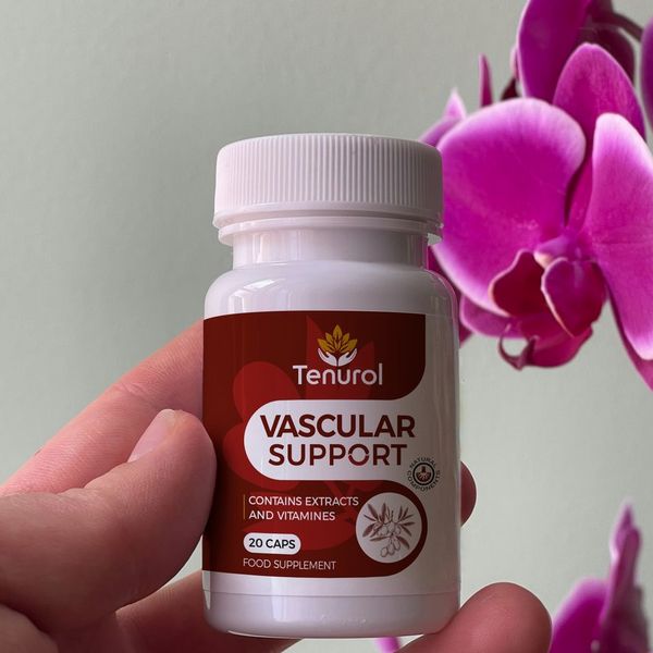 Prsty držia fľaštičku Tenurol pred sivozelenou stenou, vedľa nej sýtoružové kvety orchidey