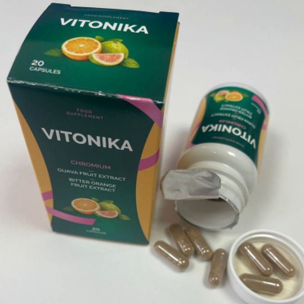 Tmavozelená krabička Vitonika, ležiaca otvorená dóza s odtrhnutou fóliou a hnedé kapsuly vo viečku a na bielom stole